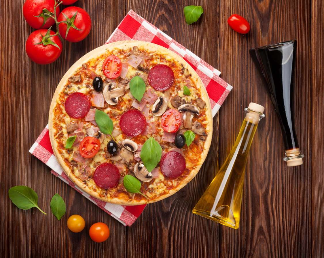 Pizza szalámival, bazsalikommal és olajbogyóval egy fából készült asztal puzzle online fotóról