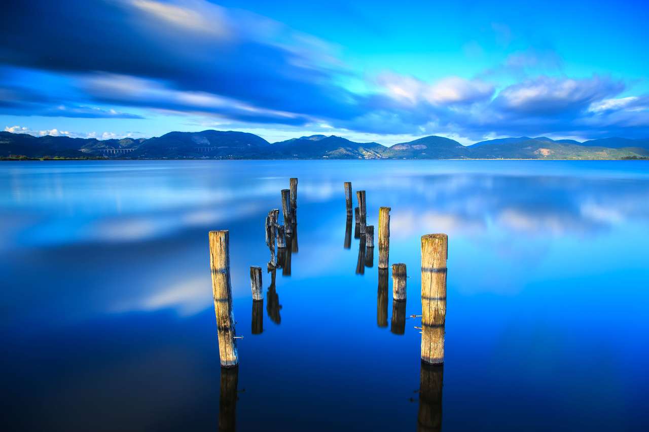La jetée en bois ou la jetée reste sur le coucher du soleil sur le lac bleu puzzle en ligne