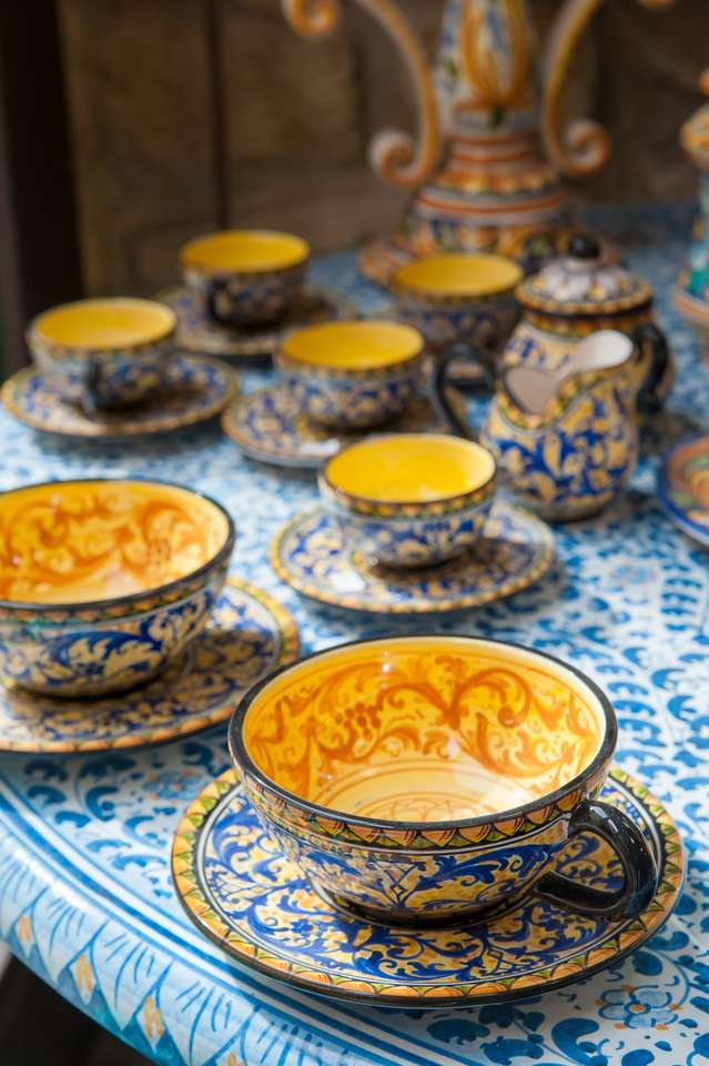 Vista aproximada de uma xícara de chá de cerâmica decorada à venda na mesa de uma oficina de cerâmica em Caltagirone, Sicília puzzle online a partir de fotografia